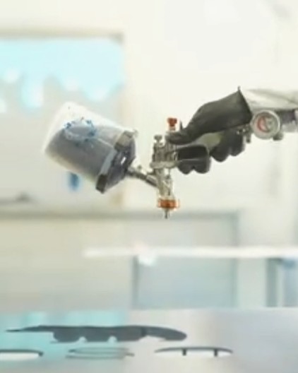 Spray gun held above sign components in an enclosed work area
