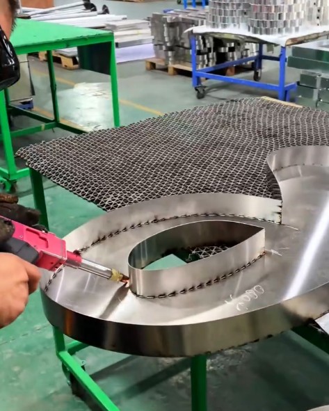 Tool joining curved metal letter components on a workshop table